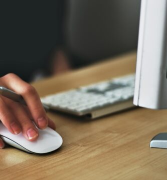 A hand using a wireless mouse at a modern desk setup with a computer and keyboard.
